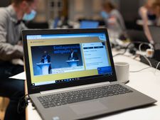 Ein Laptop im Vordergrund bei der Fachkonferenz Teilgebiete am 17. und 18. Oktober 2020 und Menschen im Hintergrund, die arbeiten.