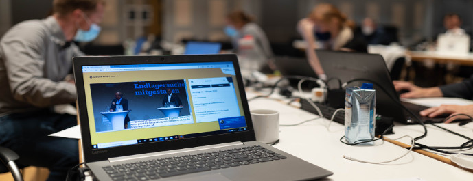 Ein Laptop im Vordergrund bei der Fachkonferenz Teilgebiete am 17. und 18. Oktober 2020 und Menschen im Hintergrund, die arbeiten.