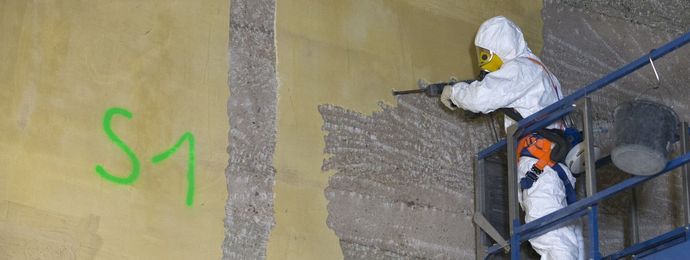 Ein im Schutzanzug gekleideter Mann trägt die Oberfläche der Wand ab (© EWN GmbH) Ein im Schutzanzug gekleideter Mann trägt die Oberfläche der Wand ab
